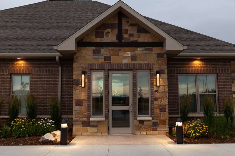 Front entrance of Owen Oral & Implant Surgery showcasing decorative stone and brick facade with glass doors and warm exterior lighting.