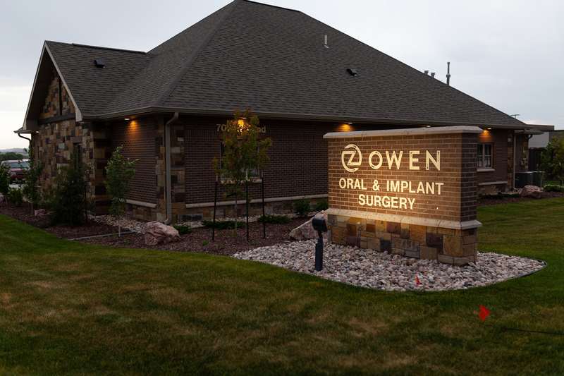 Illuminated monument sign for Owen Oral & Implant Surgery displayed on stone pillar in front of the building with landscaped grounds.