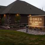 Illuminated monument sign for Owen Oral & Implant Surgery displayed on stone pillar in front of the building with landscaped grounds.