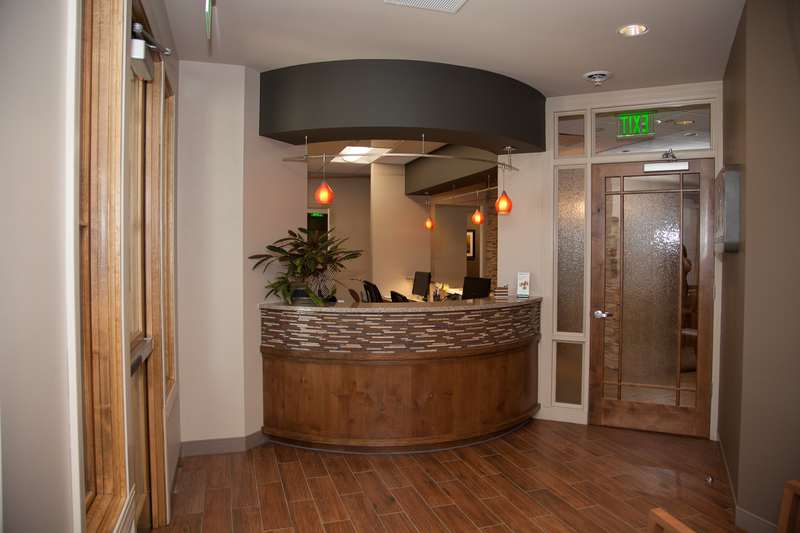 Welcoming reception area featuring a curved wooden desk with stone accents, hardwood flooring, and modern lighting fixtures.