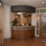 Welcoming reception area featuring a curved wooden desk with stone accents, hardwood flooring, and modern lighting fixtures.