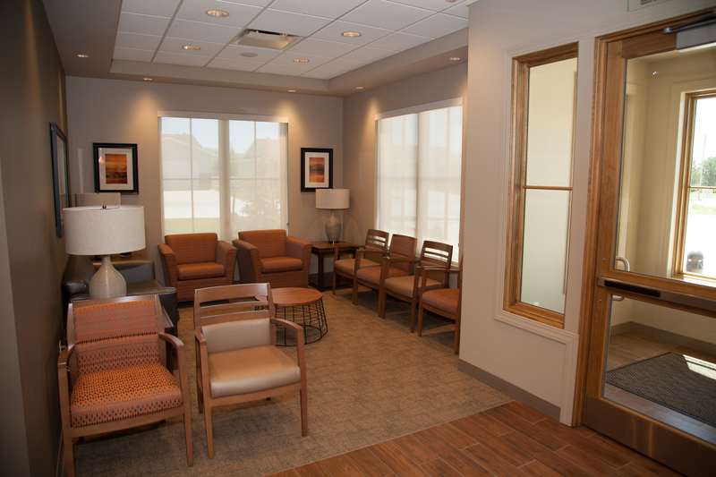 Comfortable patient waiting area with leather chairs, large windows, warm wood tones, and framed artwork on walls.