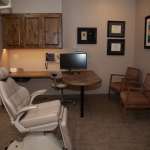 Modern dental treatment room equipped with white patient chair, computer workstation, cabinetry, and framed artwork.